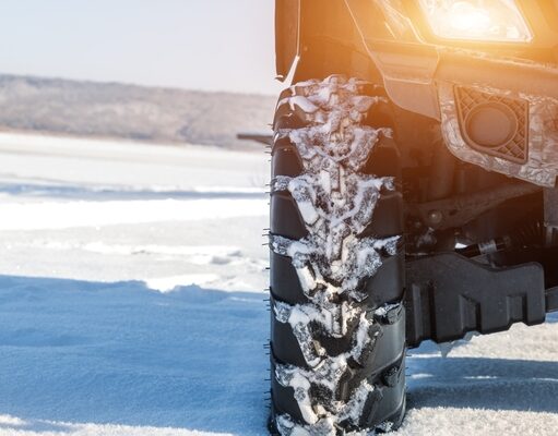 Stačí na zimu štvorkolku zakryť plachtou? Štvorkolka zakrytá plachtou, pripravená na zimu, stojí na zasneženom dvore.