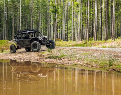 Stroje nielen pre drsňákov – štvorkolky zvládne aj začiatočník Terénna štvorkolka zaparkovaná pri lesnej ceste s odrazom v kaluži vody, obklopená vysokými stromami.